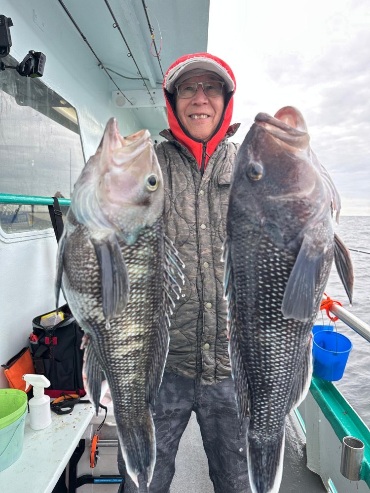 Person in a red hoodie holding two large fish on a boat.