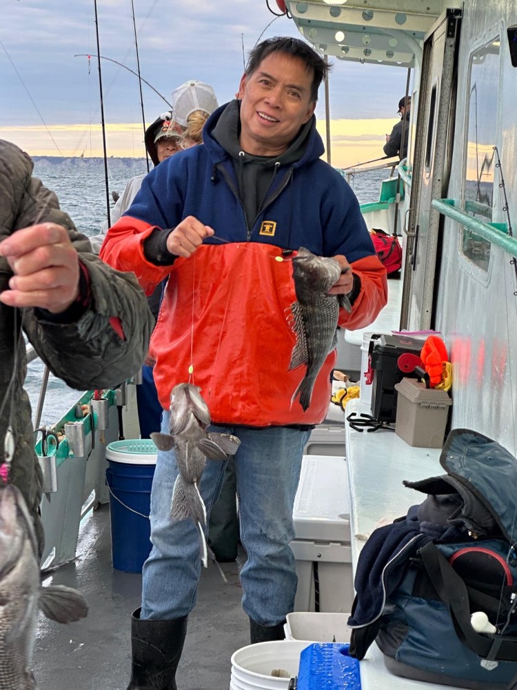 Person on a boat holding fish, with ocean and fishing gear visible.