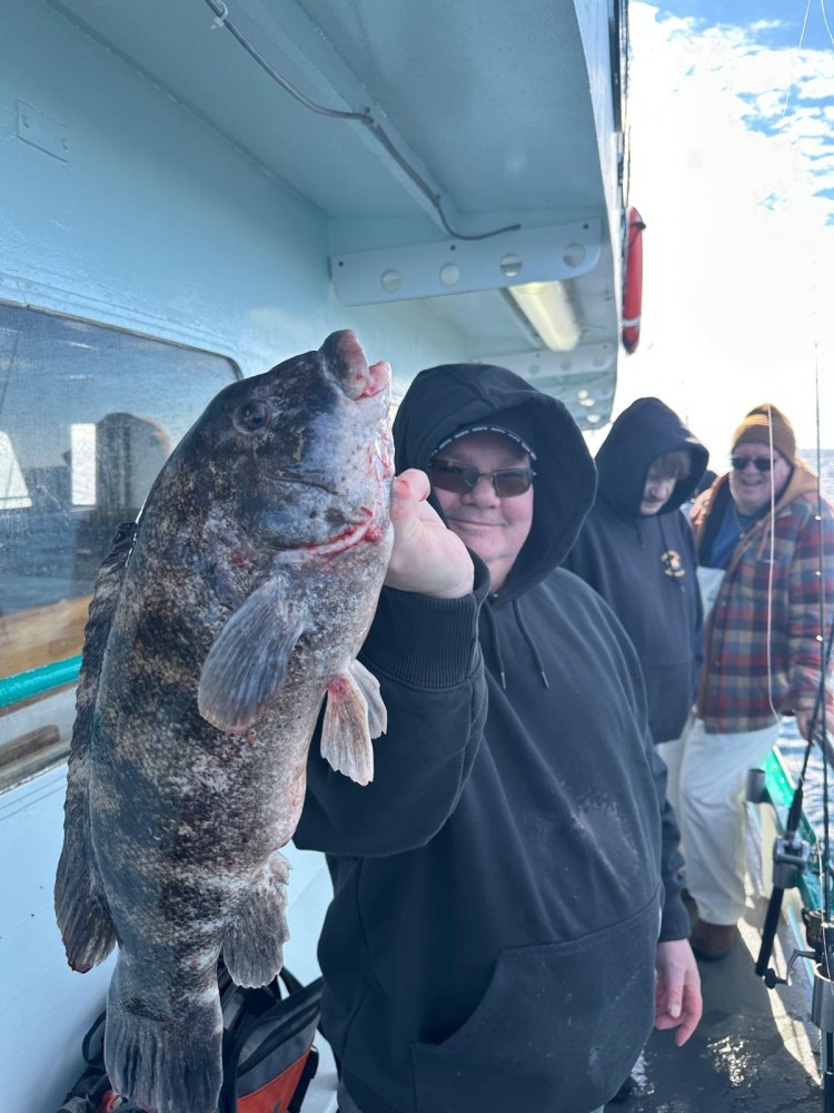 Person in hoodie holding large fish on a boat with two others in the background.