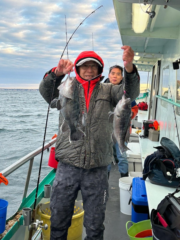 Person in winter gear holding two fish on a boat with another person and fishing gear.