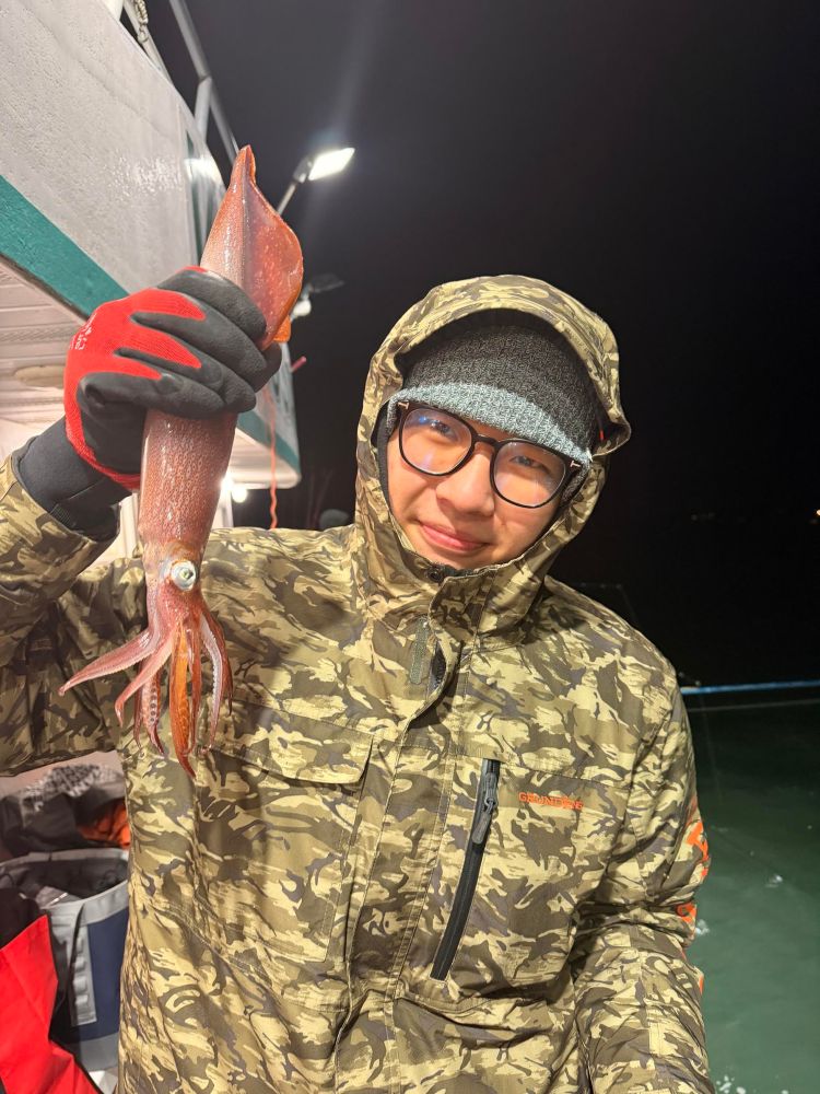 Person in camo jacket holds a squid on a boat at night.