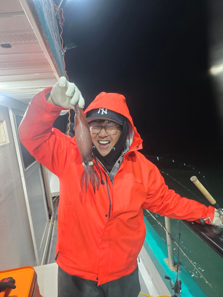 Person on a boat holding a squid, wearing an orange jacket and smiling.