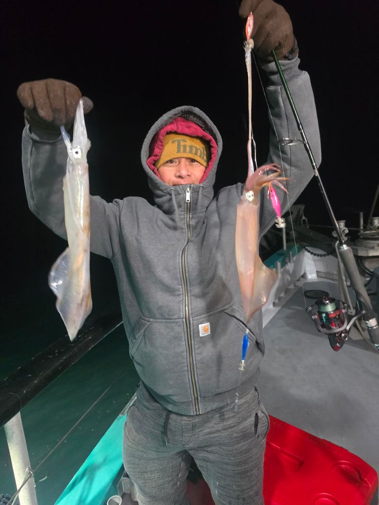 Person in winter clothing holding two squid on a boat at night.