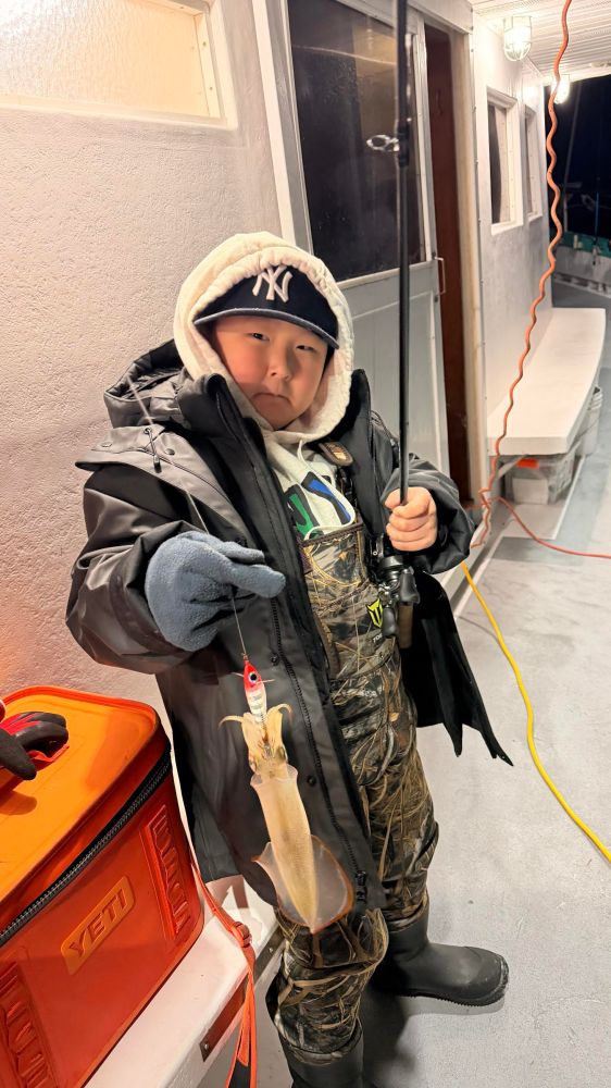 Child in warm clothing holding a fishing rod with a caught squid on a boat.