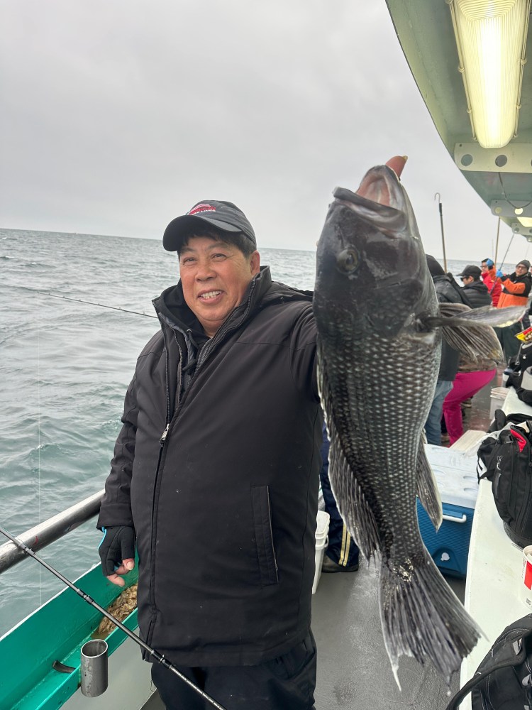 Person holding a large fish on a boat with ocean in the background.
