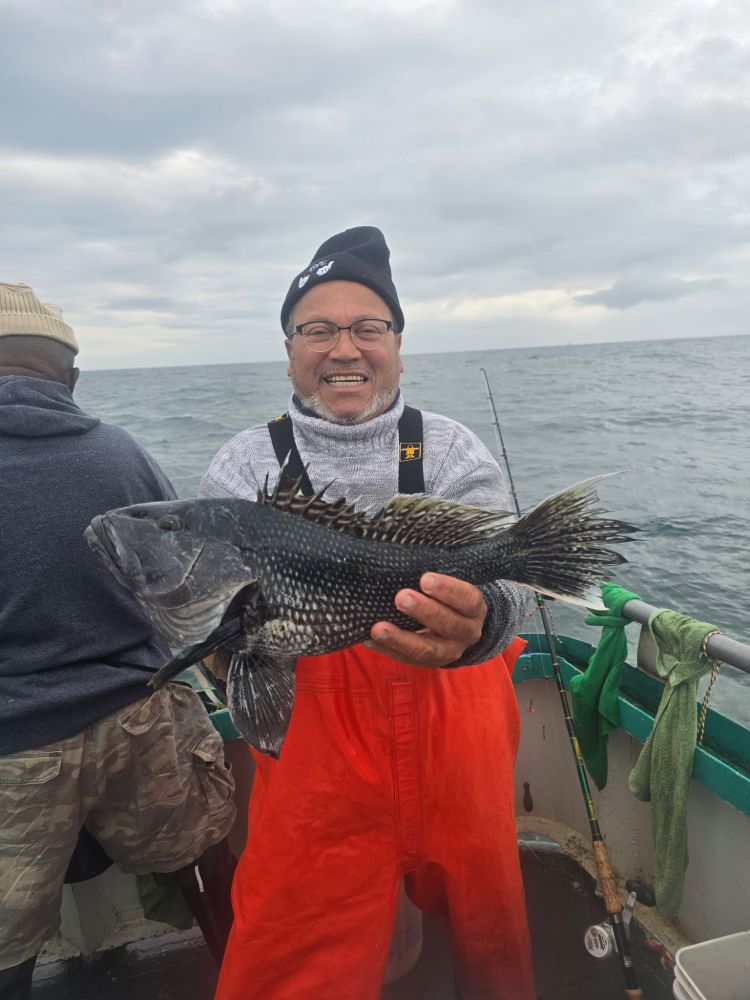 Man in orange overalls holding a fish on a boat with overcast sky.