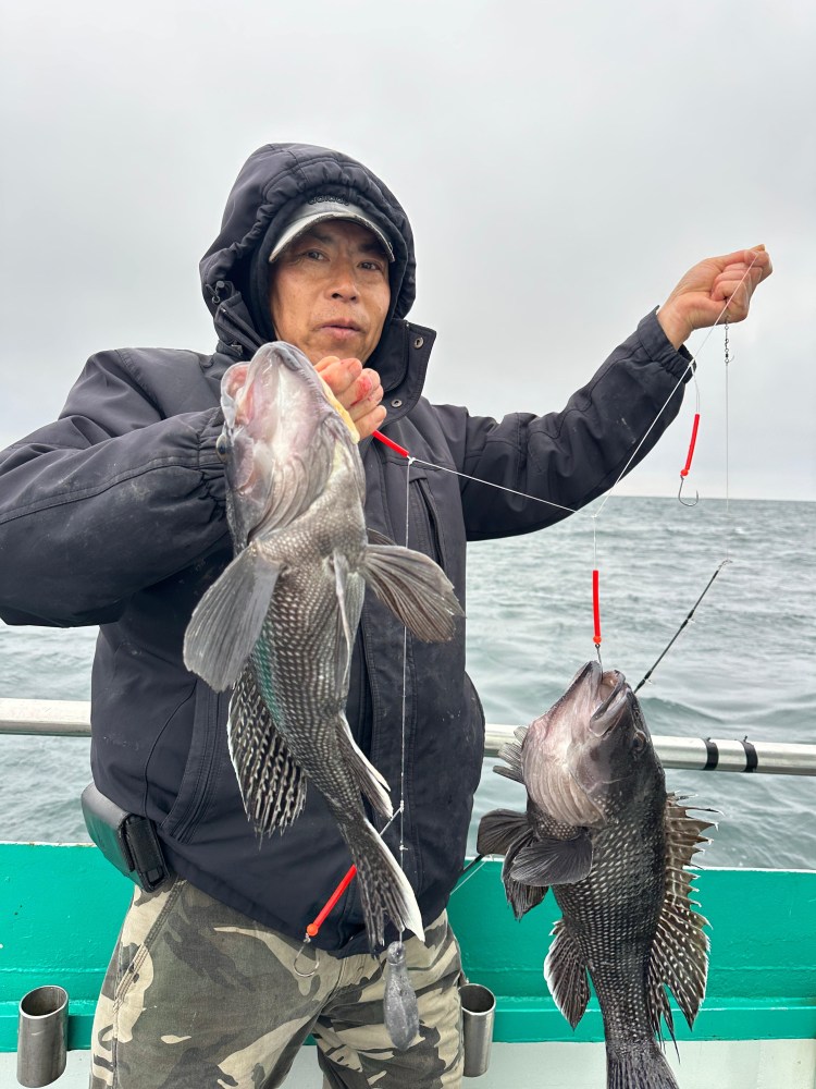 Person in a hood holds two fish on a boat overcast day.