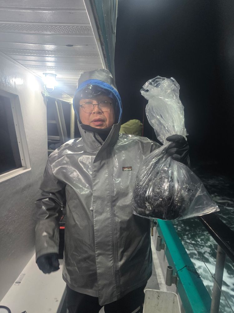 Person in raincoat holding a plastic bag on a boat at night.