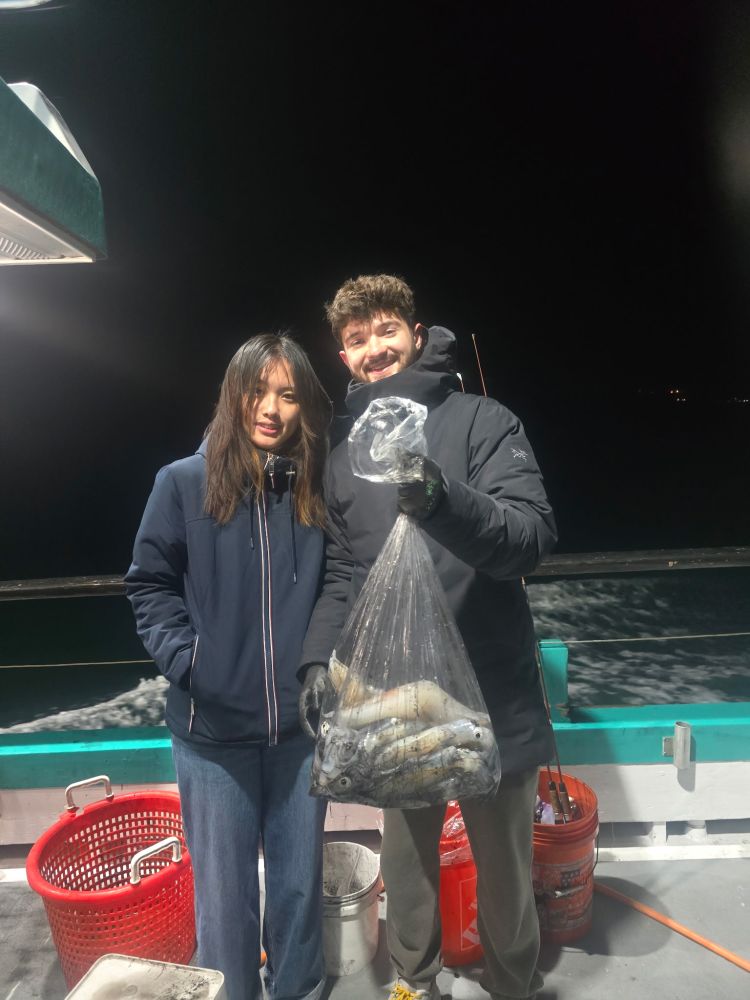 Two people holding a bag of fish on a boat at night.