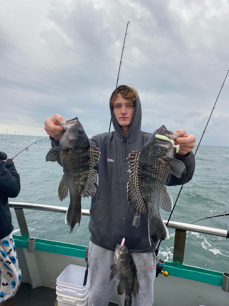 Person on boat holding two fish with ocean and fishing rods in the background.