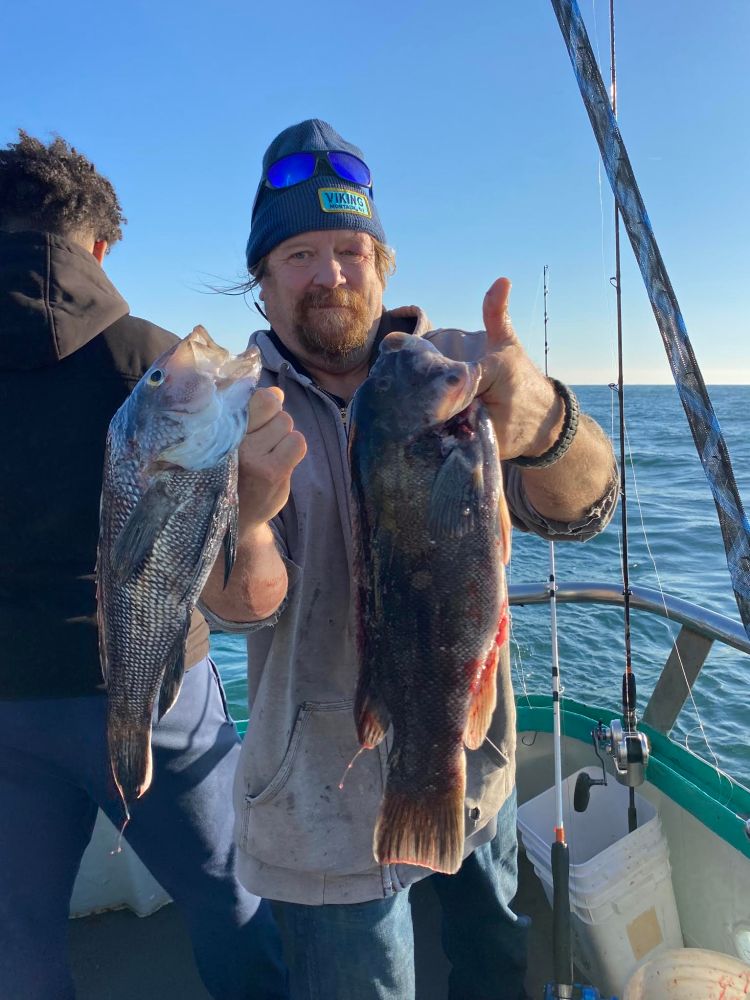 Man on a boat holding two fish with ocean in the background.