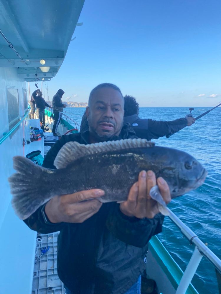 Person holding a large fish on a boat with others fishing in the background.