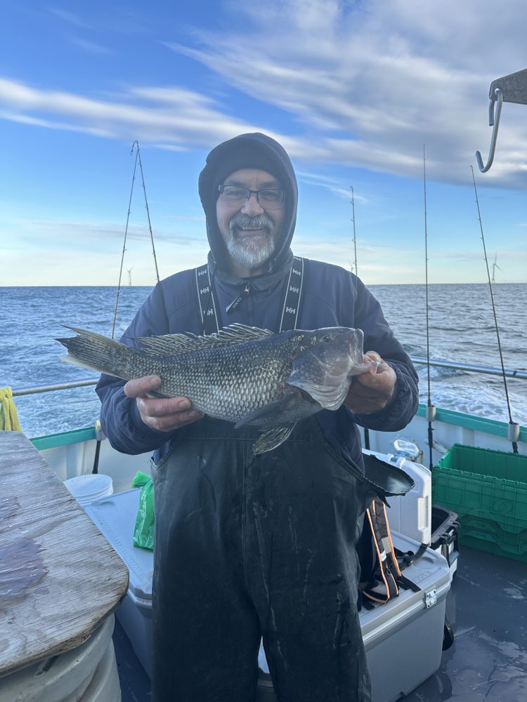 Smiling person on a boat holding a large fish, with fishing rods and sea in the background.
