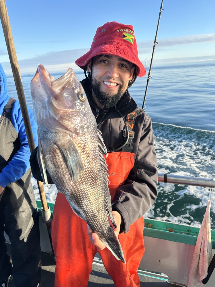 Person in red hat and gear holding a large fish on a boat.
