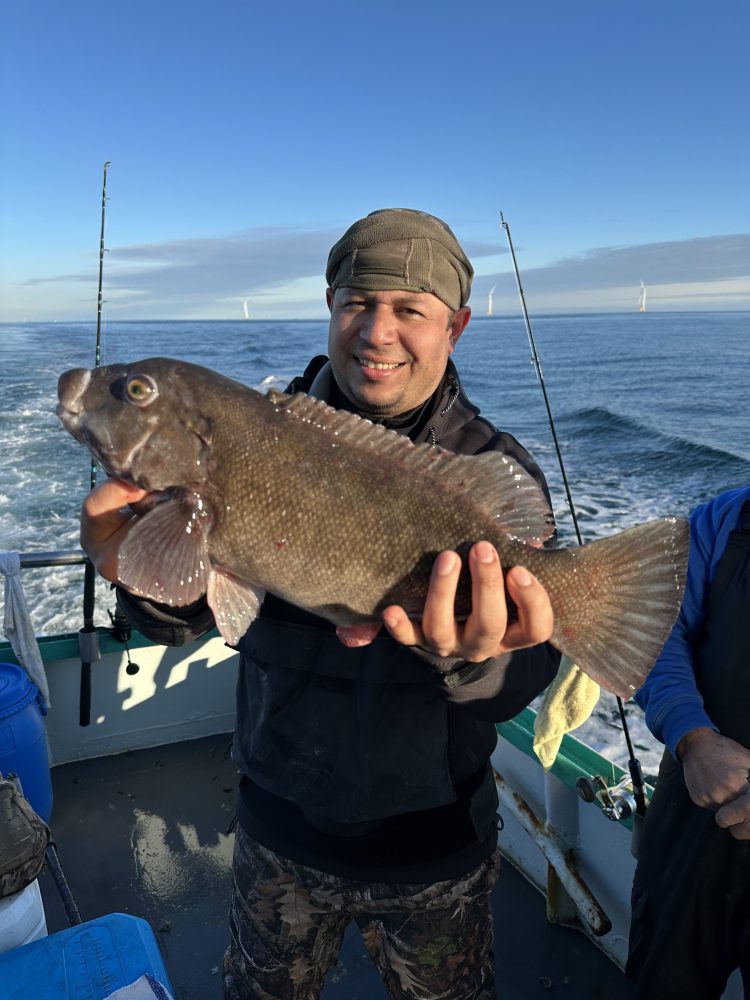 Person on a boat holding a large fish with the ocean in the background.