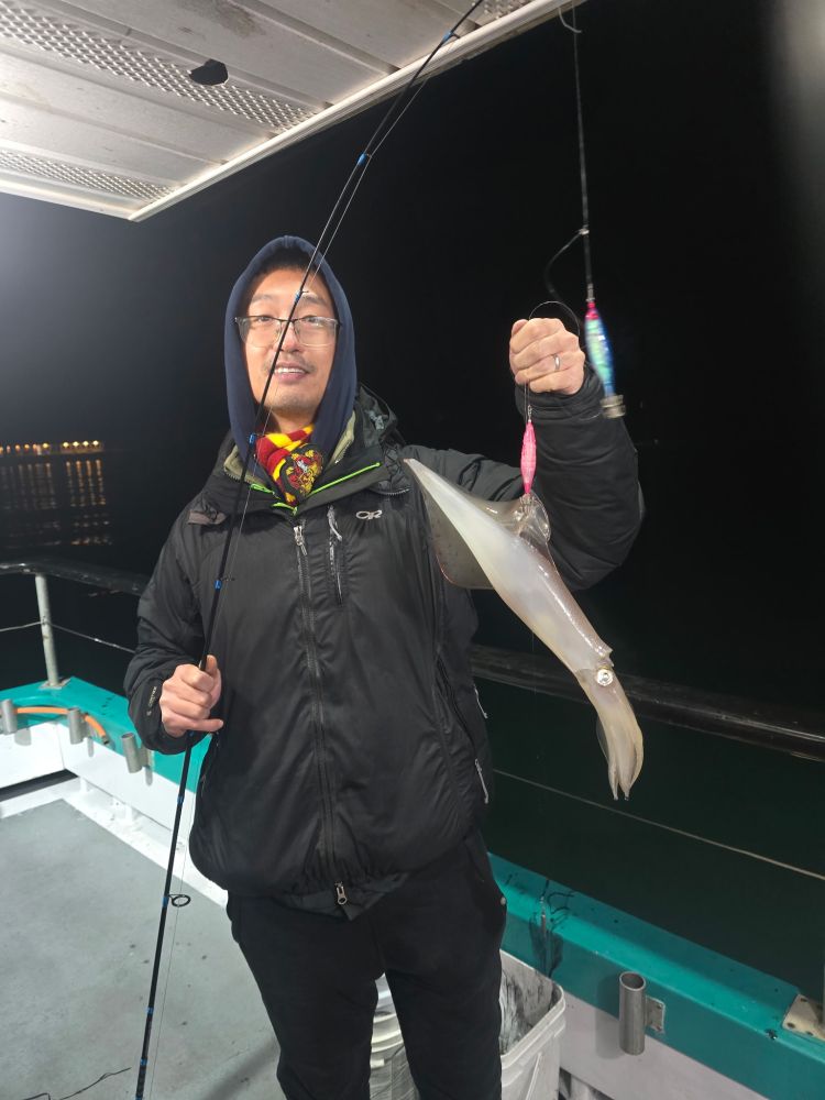 Person on a boat holding a fishing rod with a squid caught on the line at night.