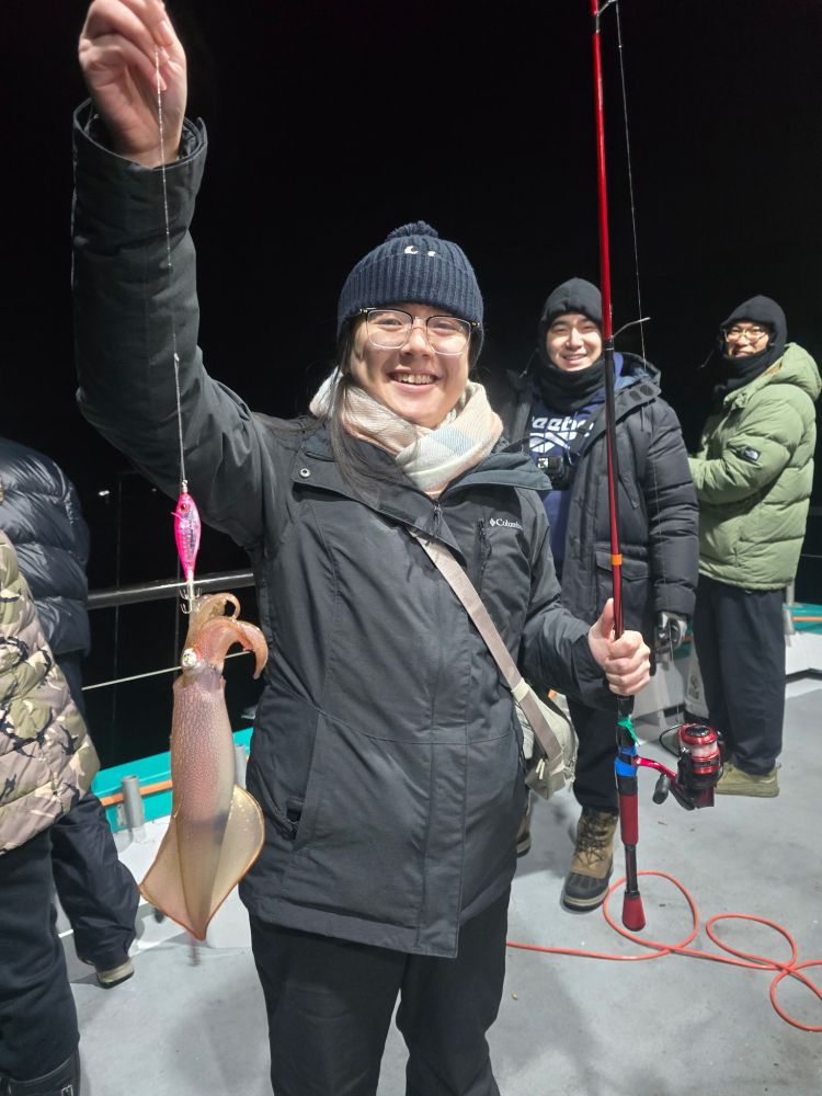Smiling person holding a squid on a fishing line at night, with others in winter clothing nearby.