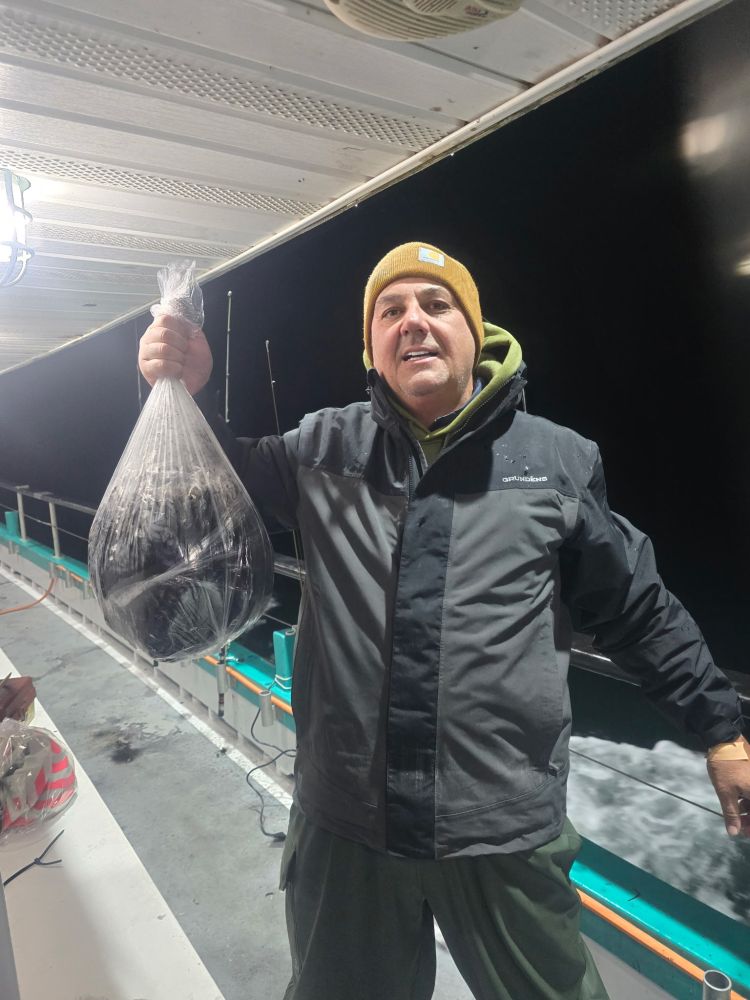 Person on a boat holding a plastic bag with fish inside at night.