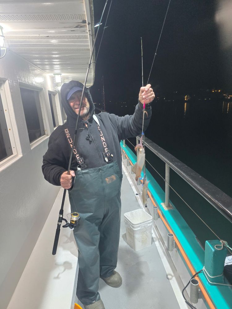 Person in fishing gear on a boat at night holding fishing rod and fish.