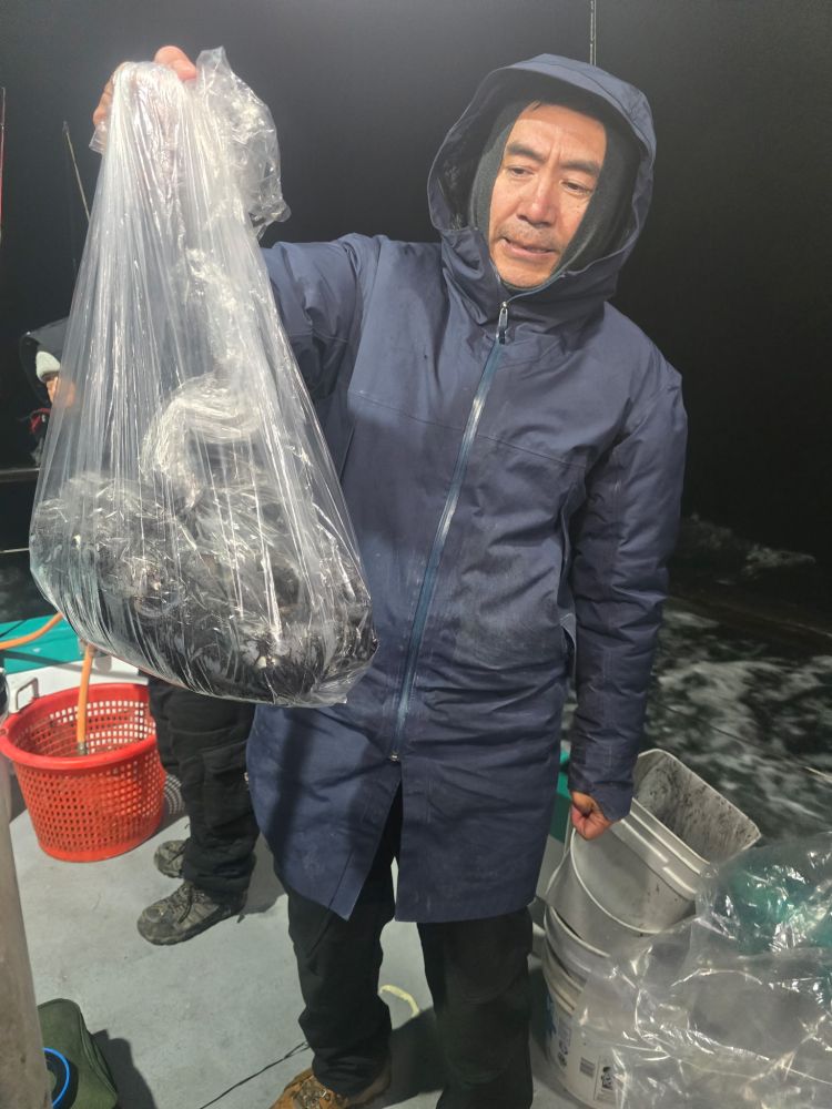 Person in a hood holding a plastic bag with contents on a boat at night.
