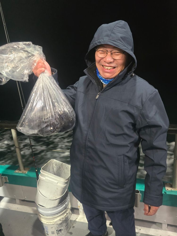 Person in a dark jacket smiling, holding a bag of fish on a boat at night.