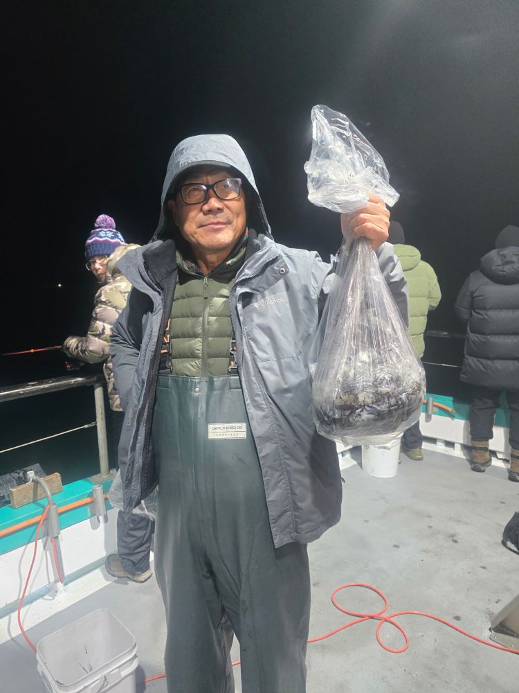 Person in a hooded jacket holds a bag of fish on a boat at night.
