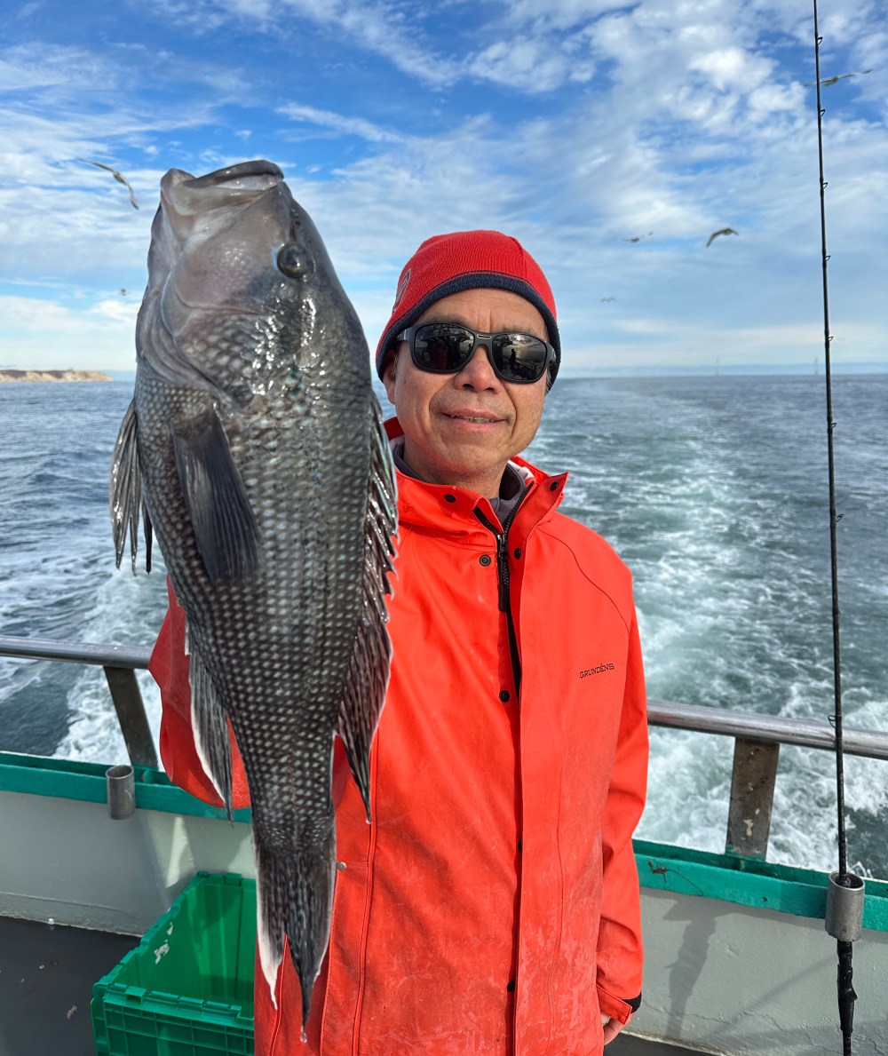 Person in red jacket holding large fish on a boat with ocean background.
