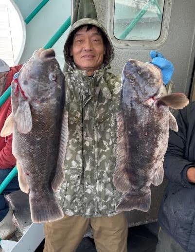 Person in camouflage jacket holding two large fish on a boat.