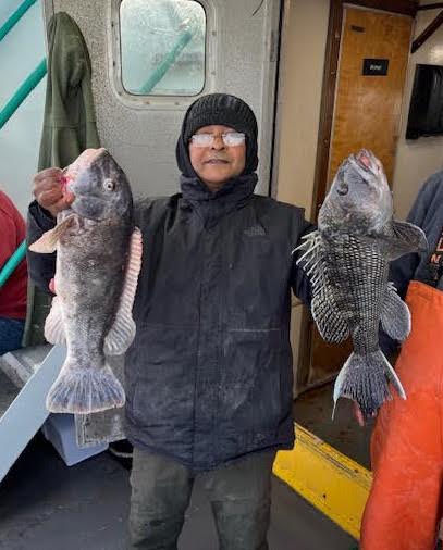 Person in winter clothing holding two large fish on a boat.