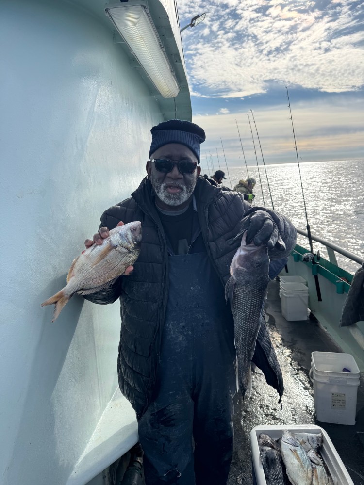 Person on a boat holding two fish, with fishing rods and sea in the background.