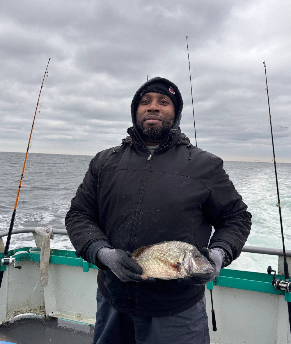 Person holding a fish on a boat, with fishing rods and cloudy sea in the background.