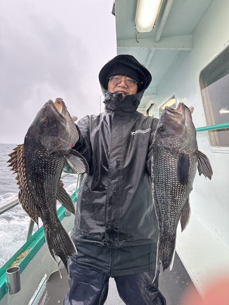 Person in rain gear holding two large fish on a boat.