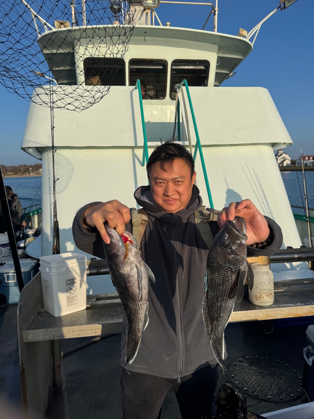 Person holding two fish on a boat deck, with the cabin visible in the background.