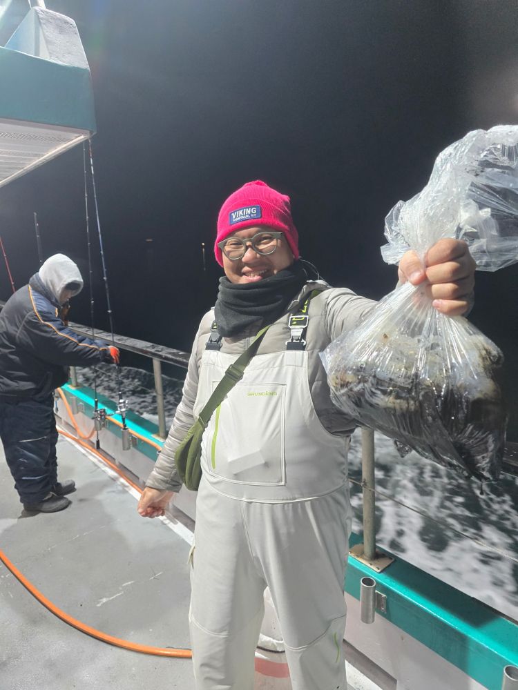 Person in white suit and red hat on a boat holding a bag of fish at night.