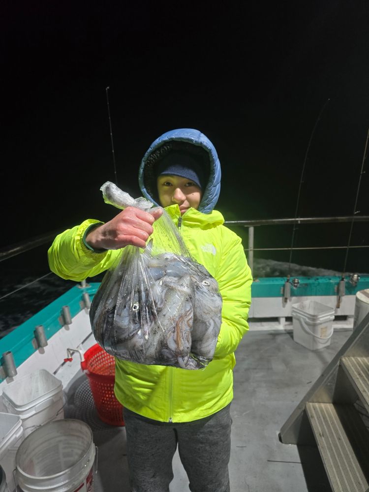 Child in a yellow jacket holding a bag of fish on a boat at night.