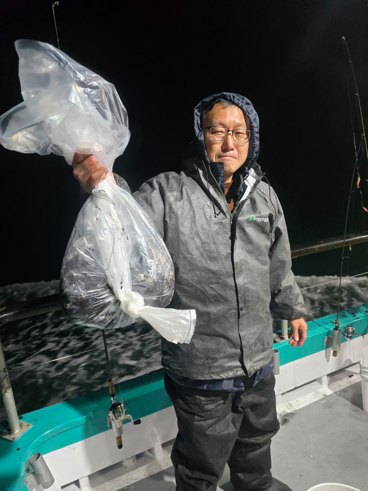 Person on a boat holding a large plastic bag with a fish inside at night.