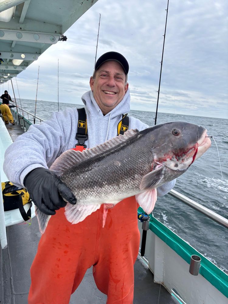 Person on a boat, smiling, holding a large fish with the ocean in the background.