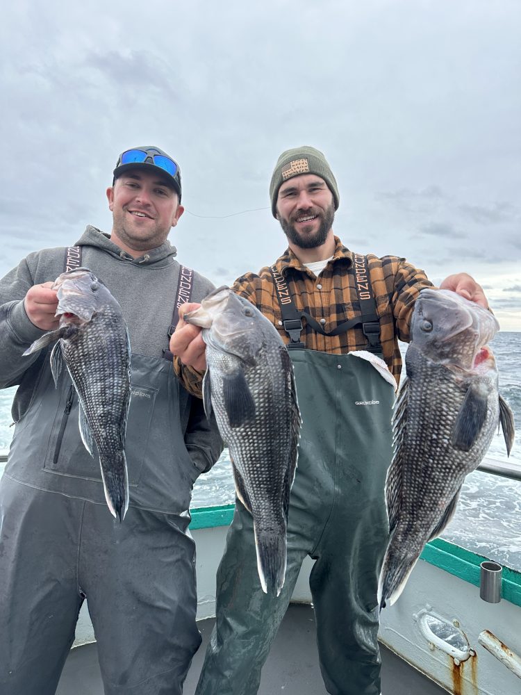 Two men on a boat smiling and holding large fish.