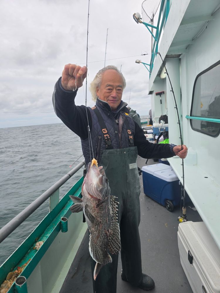Person holding a caught fish on a boat with a fishing rod, sea in background.