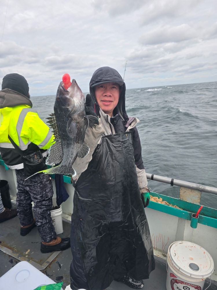 Person in black raincoat holding a fish on a boat with cloudy sky and ocean in background.