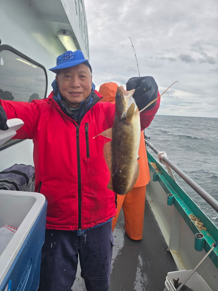 Person in red jacket and blue cap holding a fish on a boat with ocean view.