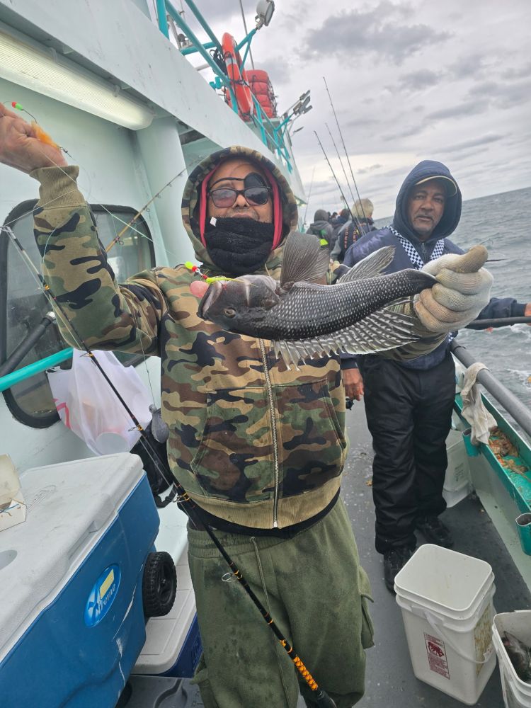 Person in camo jacket holds a fish on a boat with another person in the background.