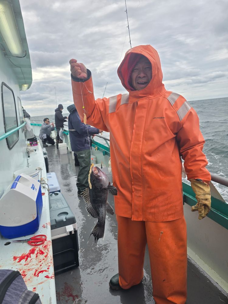 Person in orange rain gear holding a fish on a boat during cloudy weather.