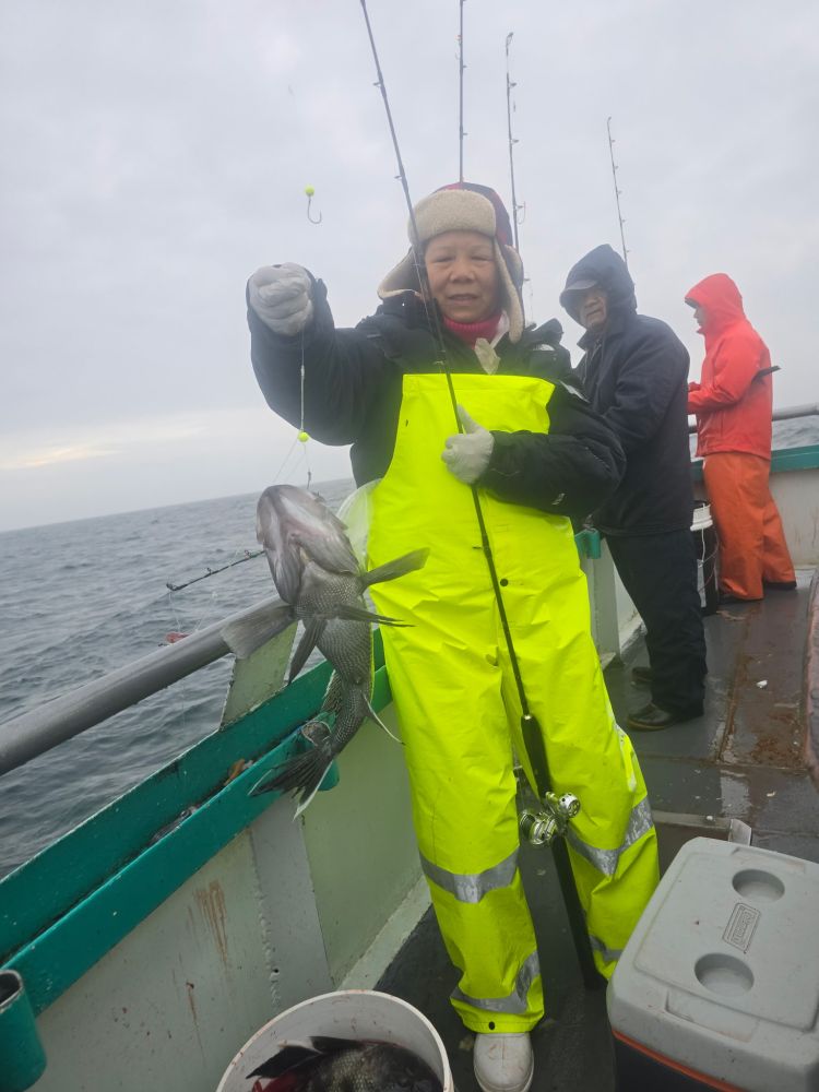 Person in yellow raincoat holds a fish on a boat with two others in the background.