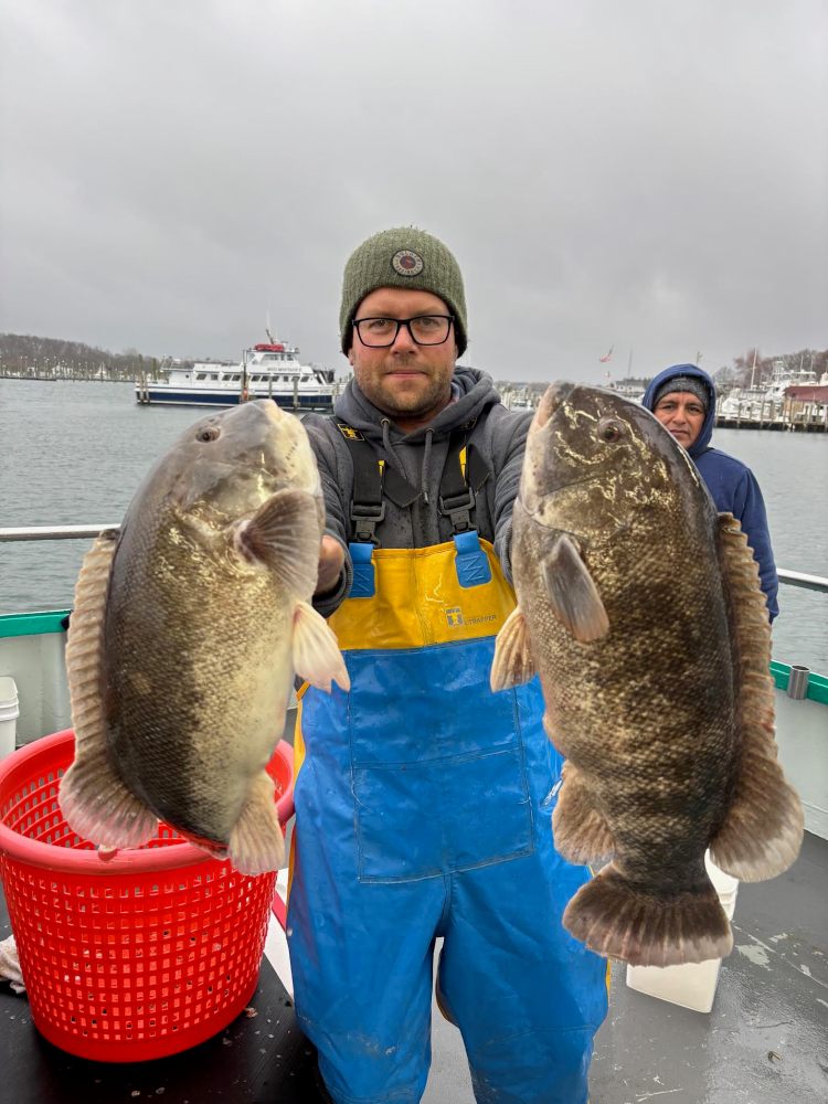 Person holding two large fish on a boat with a cloudy sky and another person in the background.