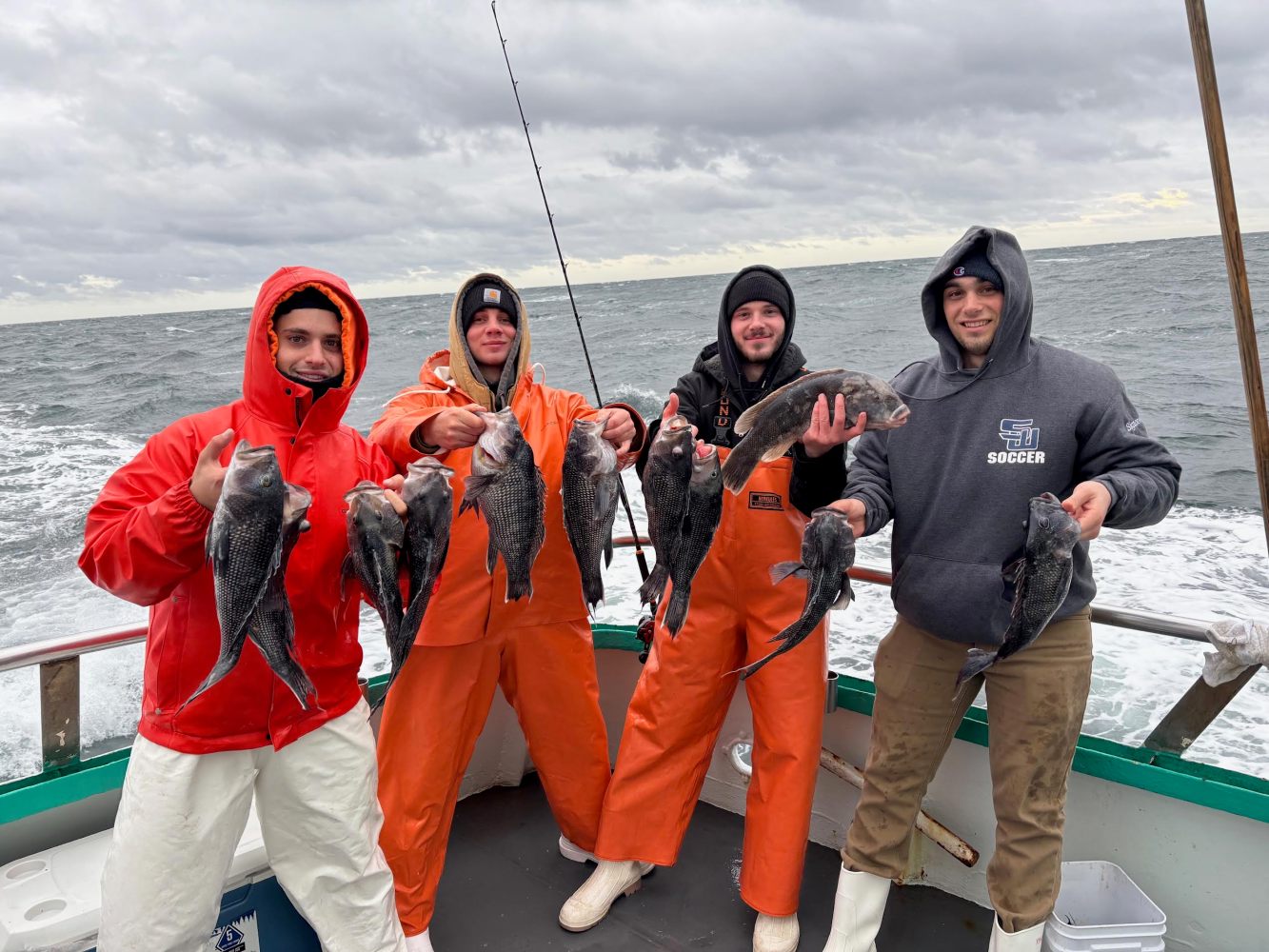 Four people on a boat holding fish with a cloudy ocean background.