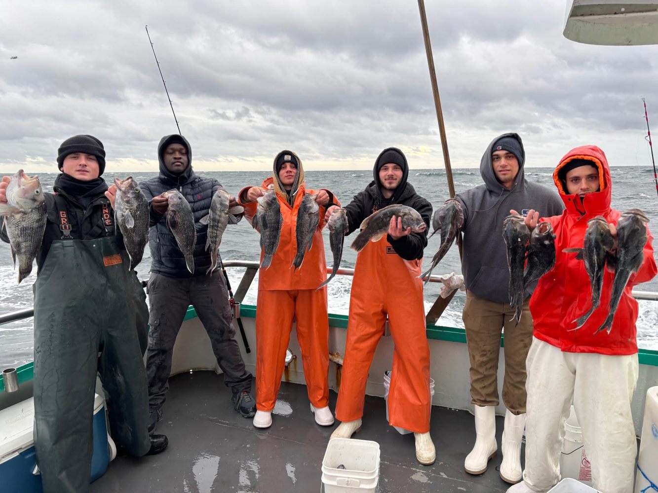 Five people on a boat holding fish, wearing winter clothing.