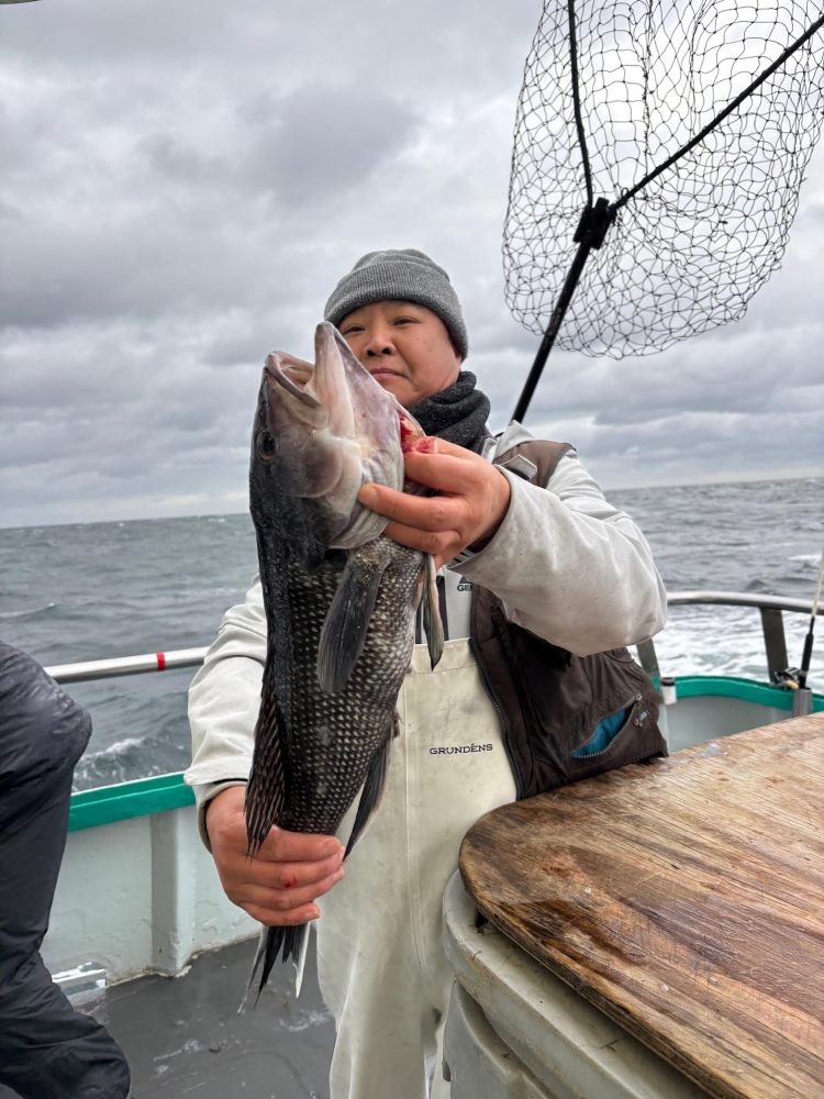 Person on boat holding a large fish with a net in the background, cloudy sky above.