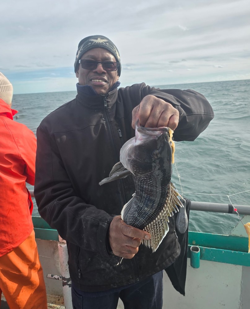 Person on a boat smiling and holding a large fish against a cloudy sky backdrop.