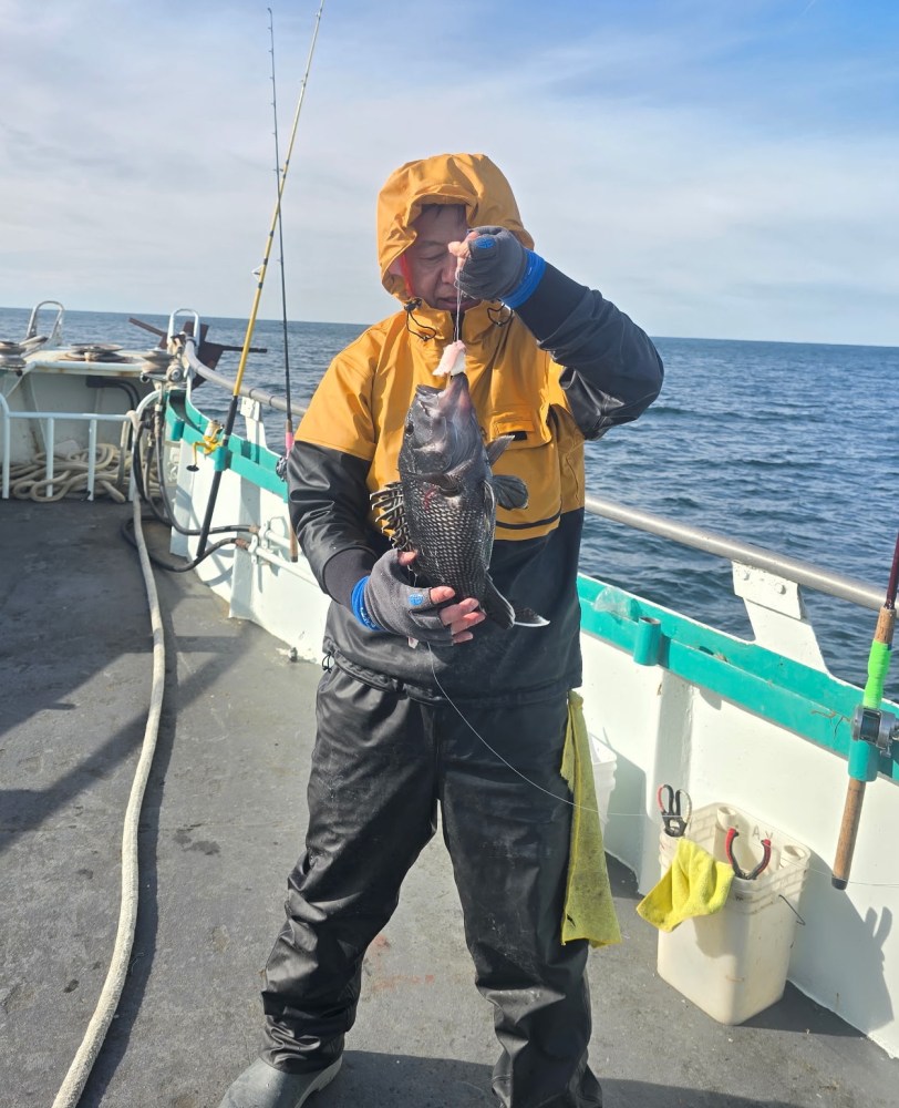 Person in yellow raincoat holding a fish on a boat with ocean in background.